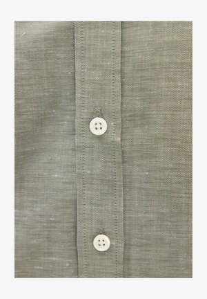 Nahaufnahme der Vorderseite eines grauen Hemdes aus Stoff mit zwei weißen Vierlochknöpfen und sichtbaren Nähten entlang der Knopfleiste.