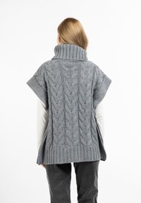 Grauer gestrickter Poncho mit einem hohen Kragen, der ein Zopfmuster aufweist und seitliche Schlitze für Bewegungsfreiheit hat. Texturiert und lässige Passform.