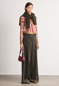 Pantalons en velours côtelé vert olive, haut à manches longues rose à motifs, écharpe verte et petit sac à main bordeaux. Chaussures dorées.