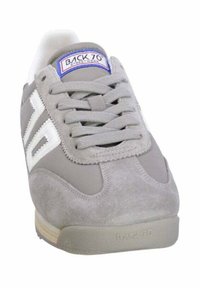 Sneaker in suede grigio con accenti bianchi, superficie testurizzata e punta rotonda. Presenta una linguetta etichettata e lacci piatti per la chiusura.