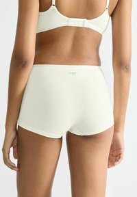 Helle, cremefarbene Baumwollshorts mit glatter Textur, ausgestattet mit einem bequemen Bund und einem kleinen Logo auf der Rückseite.