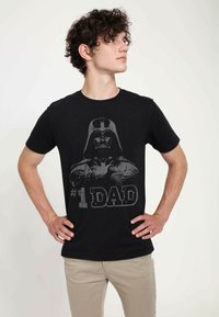 Černé bavlněné tričko s potiskem Darth Vadera a šedým textem "#1 TÁTA". Krátké rukávy, kulatý výstřih, standardní střih.