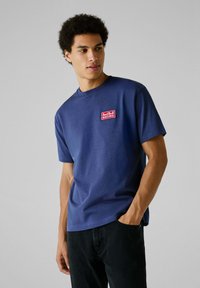 Marineblauw katoenen t-shirt met korte mouwen en een ronde halslijn, met een rood "Red Bull Racing" logo patch op de borst.