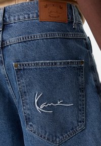 Modré džínové kalhoty s koženou nášivkou s raženým logem, bílým vyšívaným podpisem na zadní kapse a klasickými šitími detaily.