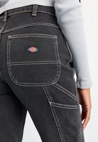 Melna denima bikses ar baltām šuvēm, kas aprīkotas ar aizmugurējo kabatu ar krāsainu Dickies logo. Šaurs piegriezums ar izsvērtām šuvēm.