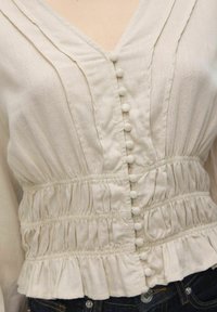 Lichtbeige blouse met een V-hals, voorzien van verticale plooien, stofbedekte knopen en een elastische gerimpelde taille met een gerimpelde zoom.