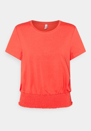 Koralgowa bluzka z krótkim rękawem, z okrągłym dekoltem i szerokim marszczonym elastycznym pasem w talii na jasnoszarym tle.