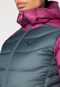 Ελαφρύ μπουφάν puffer με σκούρο τιρκουάζ σώμα και μπορντό γιακά. Περιλαμβάνει υφή με ραφές και μαύρο λογότυπο στο στήθος.