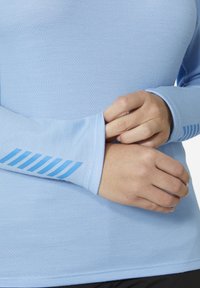 Světle modré atletické tričko s dlouhými rukávy a texturovanou tkaninou. Má otvory na palce a kontrastní modrý pruhovaný design na manžetách.