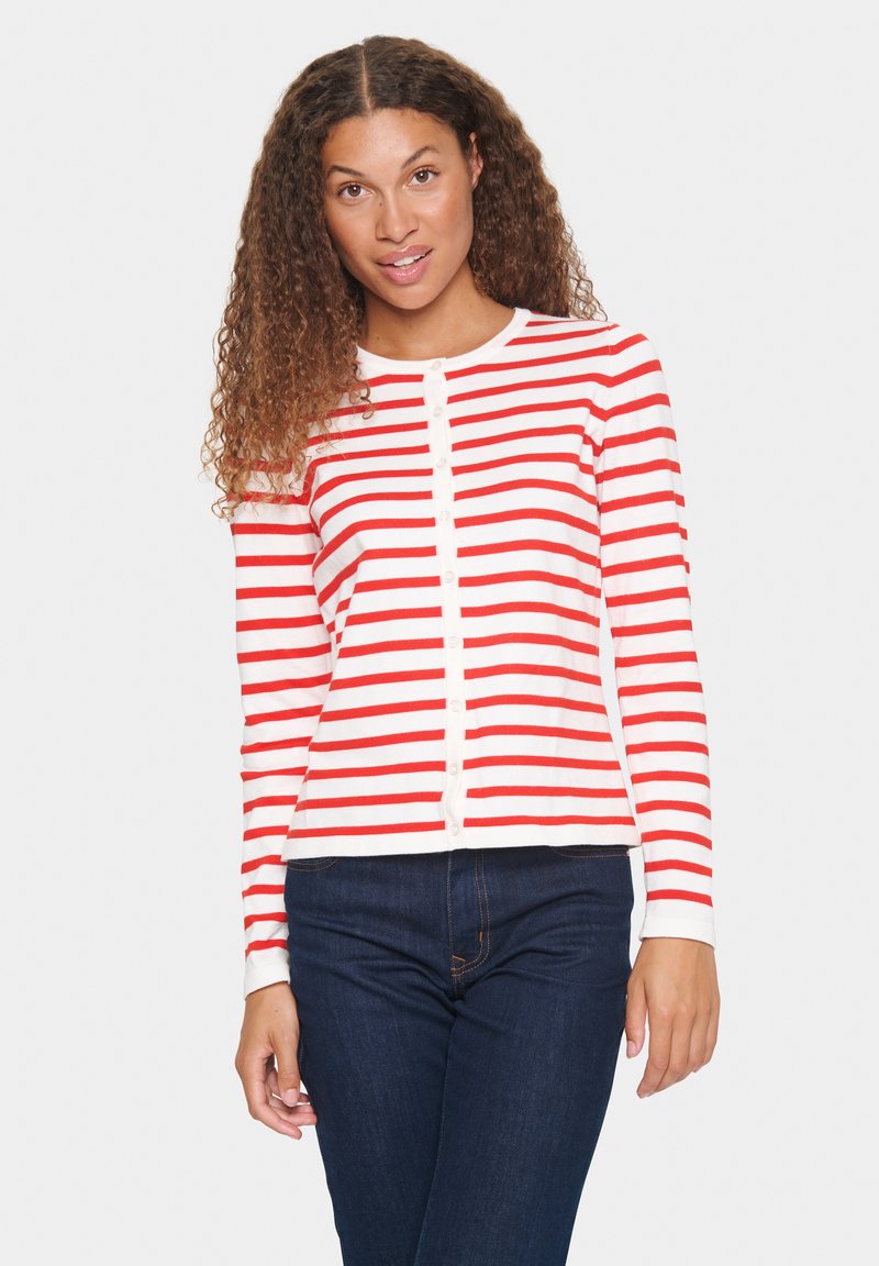 Cardigan à rayures rouges et blanches à manches longues avec un devant boutonné et un tissu doux, associé à un jean bleu foncé.