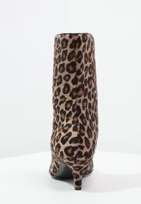 Stivale alla caviglia con stampa leopardata e un upper in pelliccia sintetica testurizzata, tacco affusolato e silhouette elegante. Suola nera e dettagli interni visibili.