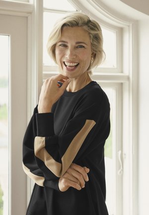 Črna bluza s svetlo rjavimi črtami na rokavih, ki se ponaša z udobnim krojem in mehkobo. Preprost, zaobljen ovratnik in dolgi rokavi.