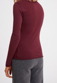 Musta pitkähihaisen paita, joka on valmistettu pehmeästä kankaasta, ja siinä on istuva malli sekä sileä pinta. Yhdistetty harmaisiin, villaisiin, kapeneviin housuihin.