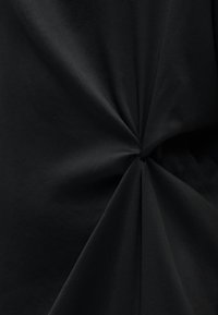 Schwarzer Stoff mit einer glatten Textur, der in der Mitte ein verdrehtes Design aufweist und dadurch dezente Falten und Dimensionen erzeugt.