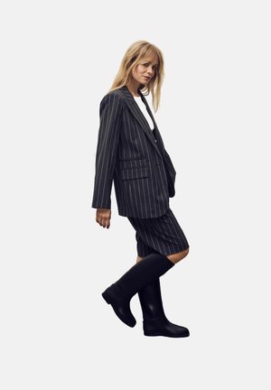 Pinstriped blazer and matching shorts in dark gray; paired with black, knee-high boots; soft texture and tailored fit.