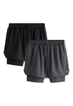 Man draagt zwarte sportshorts met daaronder compressieshorts, witte crew-sokken en zwarte Nike hardloopschoenen tegen een effen achtergrond.
