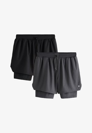 Man draagt zwarte sportshorts met daaronder compressieshorts, witte crew-sokken en zwarte Nike hardloopschoenen tegen een effen achtergrond.