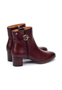 Botas de tobillo de cuero burdeos oscuro con punta redonda, tacón bajo en bloque y acentos en tono dorado en el costado. Textura suave.