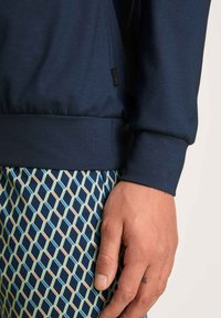 Navyblauw langemouwshirt met geribde manchetten, gecombineerd met patroon korte broek met een geometrisch ontwerp in groene, beige en blauwe tinten.