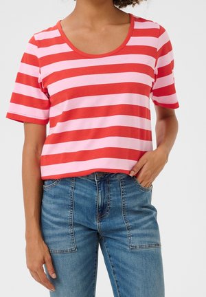 Persona che indossa una maglietta a maniche corte a righe orizzontali rosse e rosa chiaro e jeans blu a vita alta con tasche applicate davanti.
