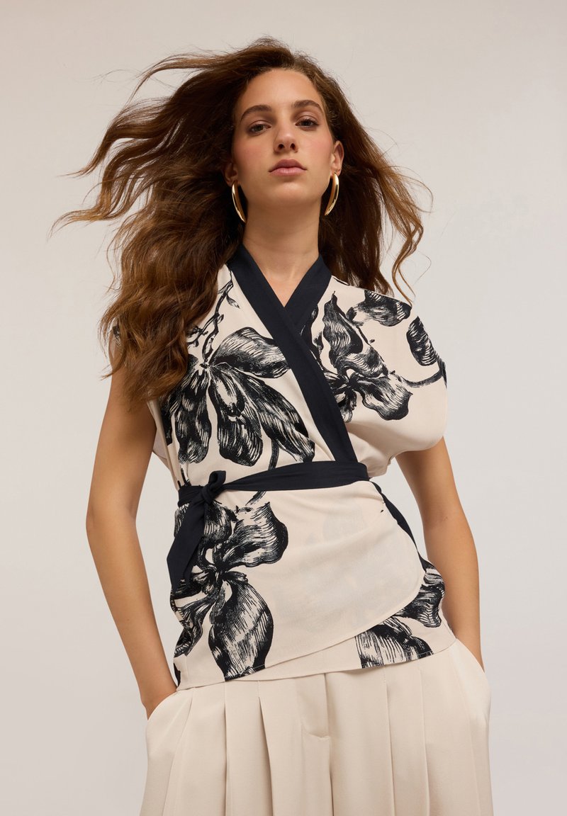 Haut à fleurs avec un imprimé botanique noir et blanc, à manches courtes et ceinture noire, associé à une jupe plissée crème.