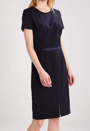 Nainen, jolla on polvenpituinen, lyhythihainen laivastonsininen mekko, jossa pyöreä pääntie ja hillitty etuhalkio.