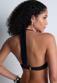 Haut de bikini noir à halter avec une lanière nouée autour du cou, présentant une texture lisse et un fermoir doré à l'arrière.