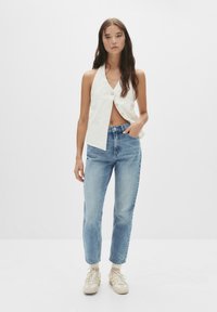 Haut sans manches blanc avec un col et des détails de boutons, associé à un jeans en denim bleu clair et des baskets beiges. Tenue simple et décontractée.