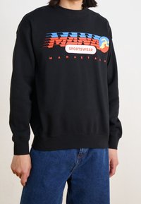 Zwarte crewneck trui met een kleurrijk grafisch ontwerp met rode, blauwe en gele accenten. Gemaakt van zachte katoen, lange mouwen, losse pasvorm.
