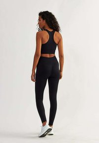 Black sports bra with a racerback design and textured pattern paired with high-waisted black leggings. Model wearing white athletic shoes.