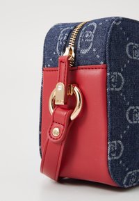 Handtasche aus Denim und rotem Kunstleder mit goldfarbenen Beschlägen, einem Reißverschluss und einem abnehmbaren Riemen. Auf dem Denim ist ein Logo-Muster zu sehen.