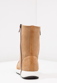 Bota de ante beige con un eje alto, cremallera lateral y costuras contrastantes. Presenta una suela blanca y una textura suave.