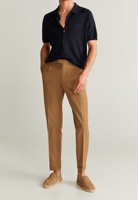 Camicia a maniche corte blu navy con bottoni, pantaloni marroni su misura dalla texture liscia e scarpe slip-on color ocra in uno stile casual e aderente.