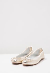 Gouden metallic ballerina's met een gladde afwerking, ronde neus en een decoratieve strik aan de voorkant. Zachte voering en platte zool.
