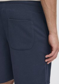 Tumesinised puuvillased lühikesed püksid küljetaskuga, elastse vöökohaga ja siledalt viimistletud, pildistatud tagantpoolt.