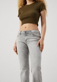 Un haut court côtelé vert olive associé à un jean droit gris clair. Le jean dispose de poches avant et d'une texture légèrement délavée.