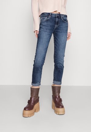 Jean en denim bleu marine avec une coupe fuselée et des ourlets retroussés, associés à des bottes compensées marron avec une doublure en fourrure et un détail de boucle.