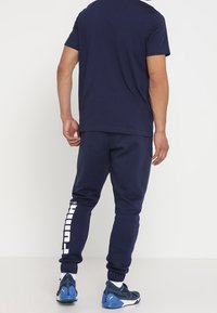 Marinblå bomullströja med korta ärmar, kombinerad med matchande joggers som har en vit "PUMA"-logotyp längs med vänster ben och elastiska slitsar.