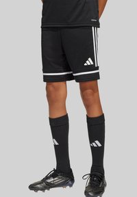 Schwarze Sportshorts mit weißen Streifen und einem Adidas-Logo, kombiniert mit schwarzen knielangen Socken und schwarzen Fußballschuhen mit silbernen Akzenten.