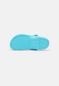 Semelle en caoutchouc bleu clair de sabot avec motif de bande de roulement texturé et logo de la marque visible au bas, sur fond blanc.