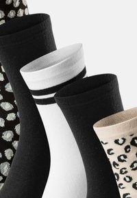 Fünf Paar Socken: zwei schwarze, eine weiße mit schwarzen Streifen, eine beige mit Leopardenmuster und eine schwarze mit gepunktetem Muster. Baumwollmischung.