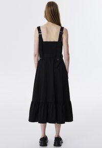 Zwarte katoen jurk met schouderbanden en een gerimpelde zoom. Voorzien van verstelbare zilveren hardware en een licht getailleerde bustier.