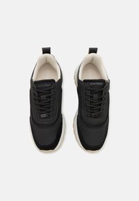 Sneakers neri con rete testurizzata e accenti lisci. Suola chiara, punta rotonda e senza loghi visibili, eccetto che sulla linguetta.
