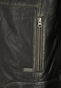 Schwarze Lederjacke mit glatter Textur, einem auffälligen silbernen Reißverschluss an der Seite und einem kleinen metallischen Markenlabel.