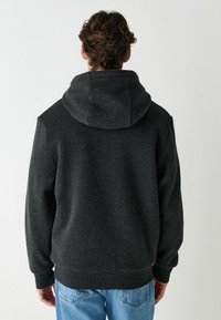Dunkelgrauer Kapuzenpullover mit weicher Textur, ausgestattet mit einer Kängurutasche und gerippten Bündchen, getragen mit hellblauen Jeans.