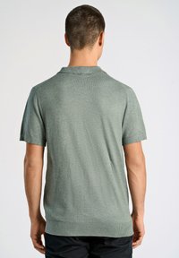 Grön kort�ärmad polo med en strukturerad stickad yta, som har en klassisk krage och ribbade muddar, visas från baksidan.