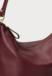 Bordo kožna torba za rame s glatkom površinom i zlatnim detaljem na zatvaraču. Ima zakrivljeni oblik i jedan remen za nošenje.