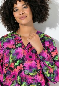 Mønstret bluse i flere farver med et blomster tie-dye mønster i pink, grøn og sort, med V-udskæring og lange ærmer. Glat stofstruktur.