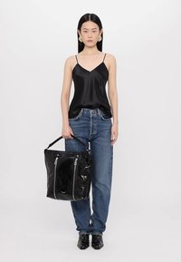 Camisole negru din satin cu bretele subțiri, purtat cu blugi albaștri. Modelul ține o geantă lucioasă neagră, cu fermoare și un mâner rezistent.