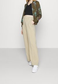 Bomber bunda s olivově zeleným květinovým vzorem, černý crop top, béžové široké pruhované kalhoty a bíl�é tenisky s červenými akcenty. Neformální souprava.